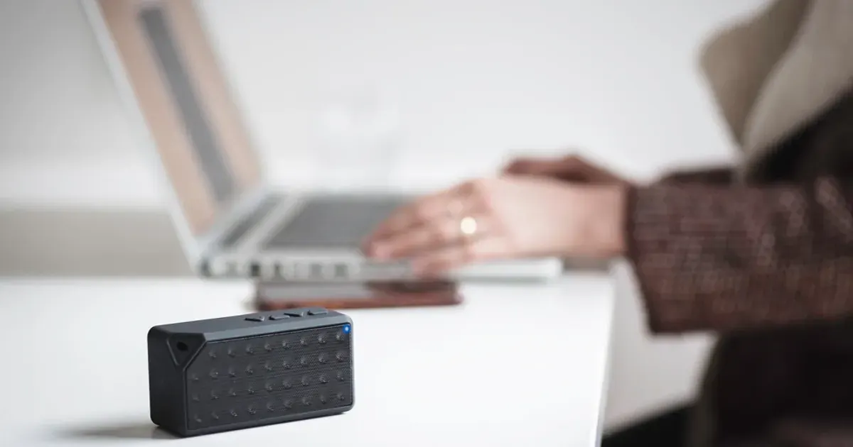Small black wireless speaker on a desk beside a laptop