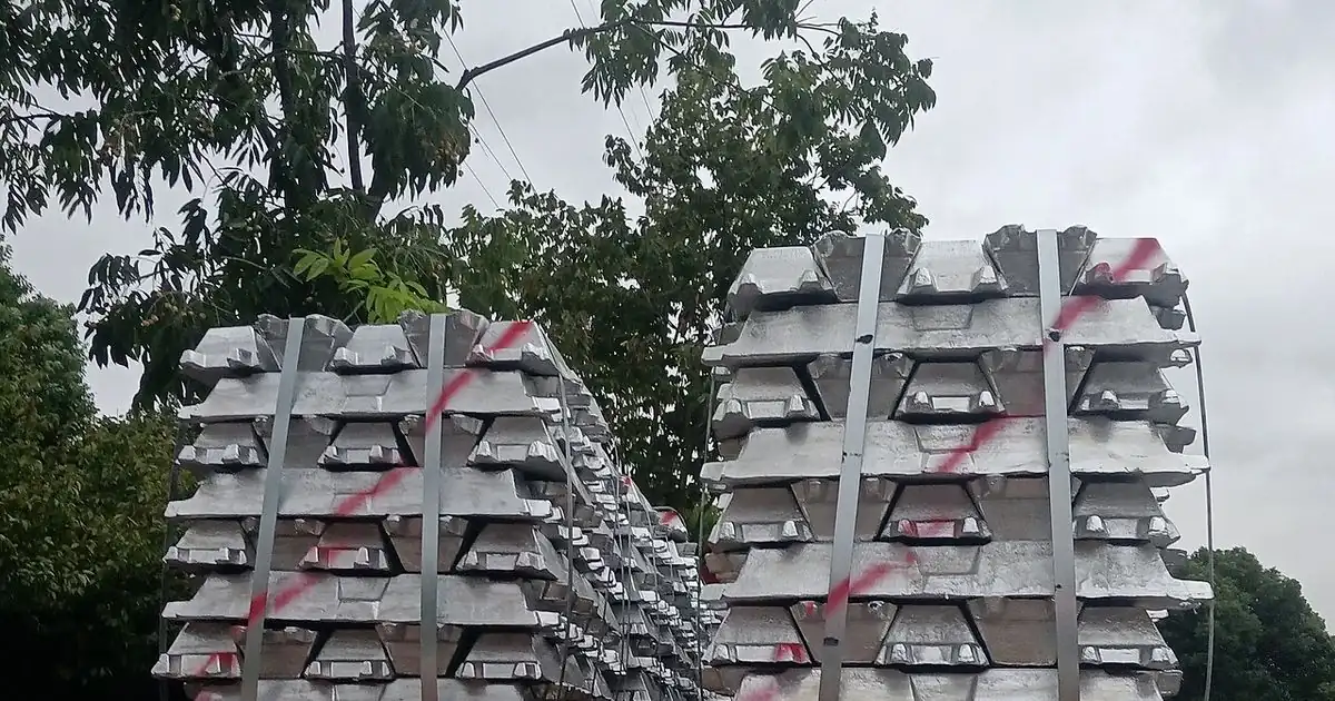 Stacks of silver aluminum ingots strapped together on a truck, with trees behind them