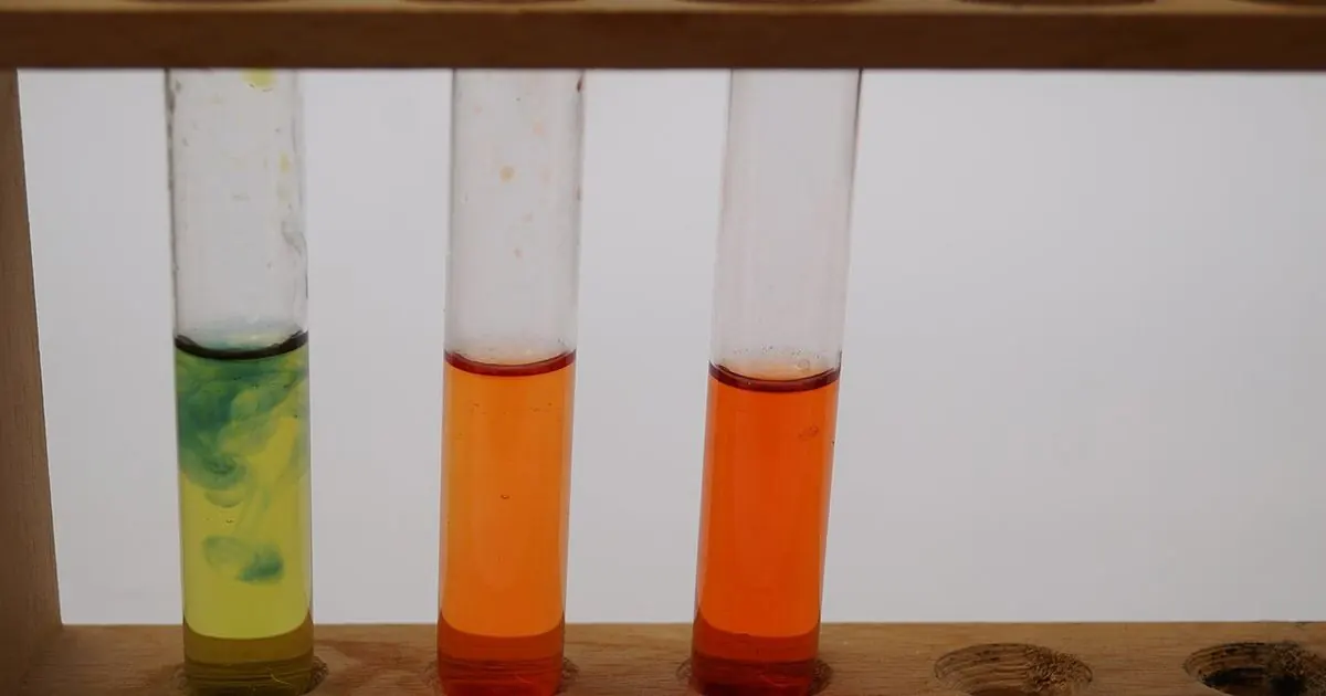 Three glass test tubes with green and orange liquids in a wooden laboratory rack
