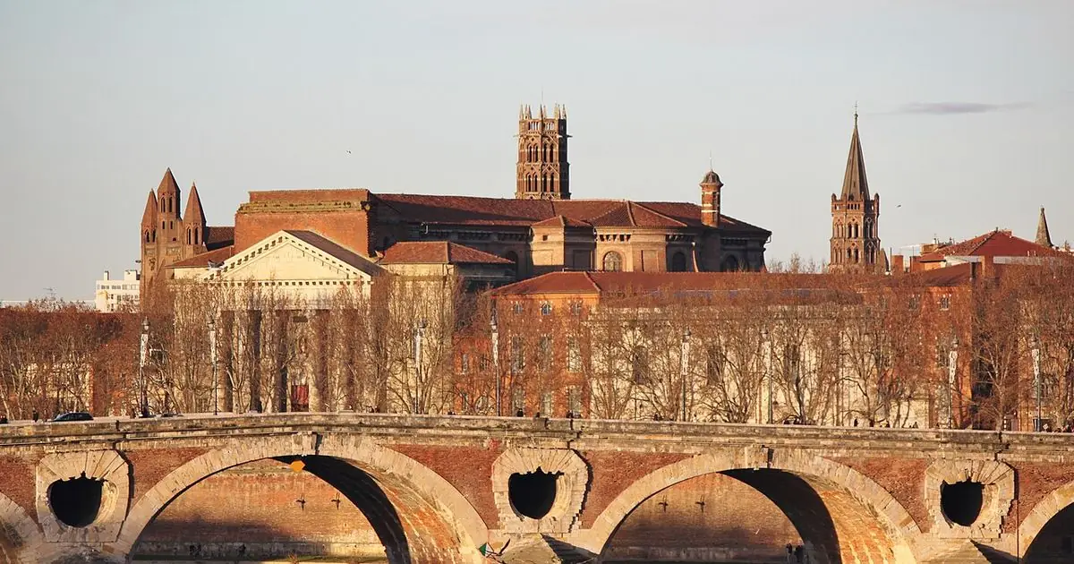 The Pont Neuf bridge over the Garonne river in Toulouse with red-brick buildings and church towers behind it