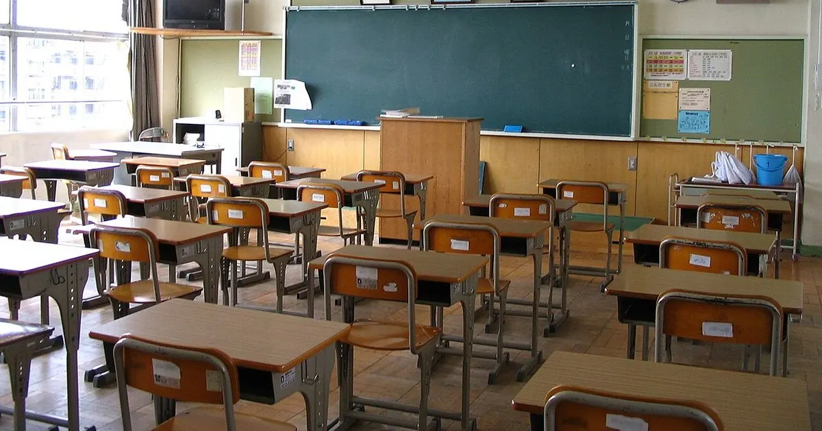 An empty school classroom with rows of wooden desks and chairs facing a green chalkboard