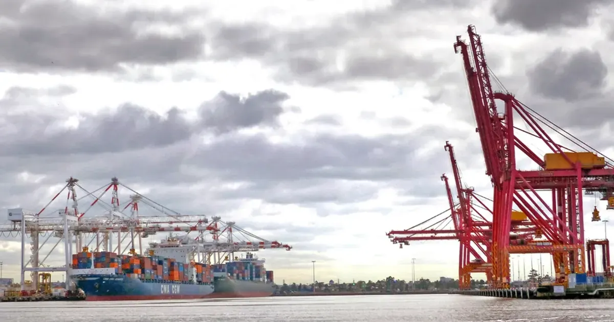 Stacked shipping containers and cranes at a busy cargo port