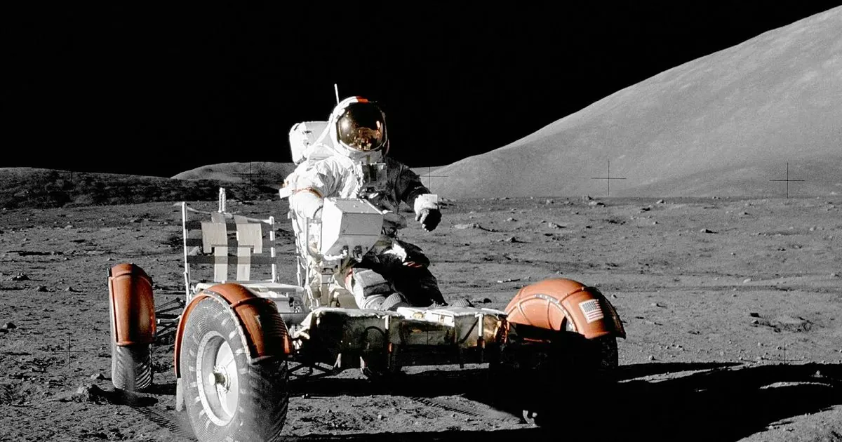 An Apollo 17 astronaut driving the lunar roving vehicle across the grey surface of the Moon