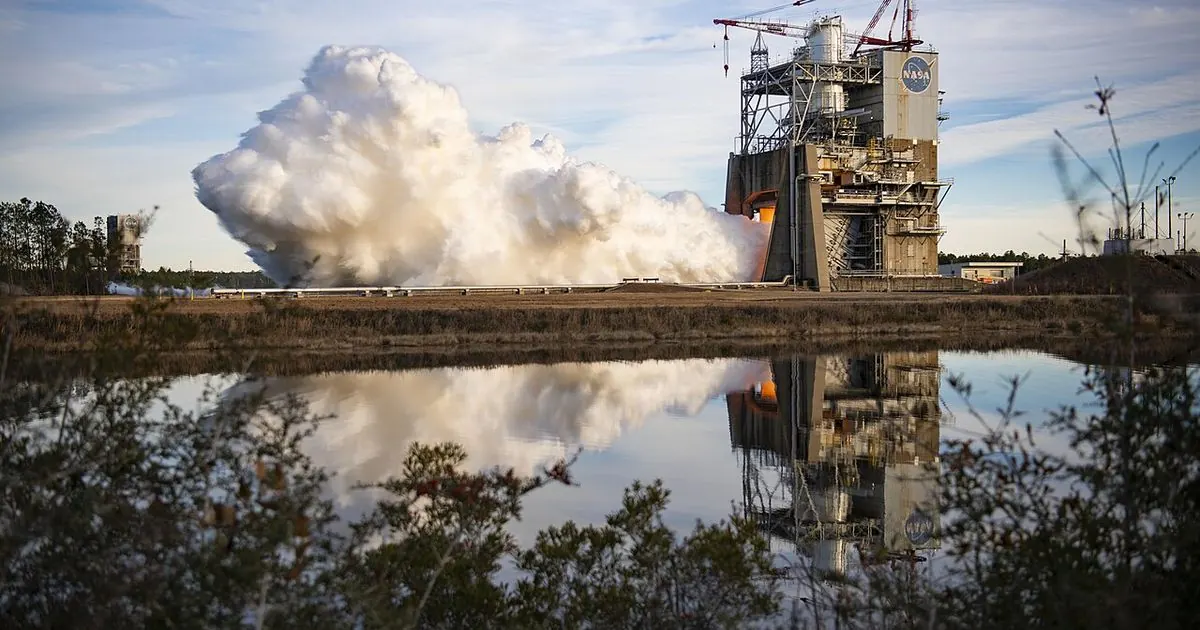 An RS-25 rocket engine firing on a test stand at NASA Stennis Space Center, with a large plume of steam