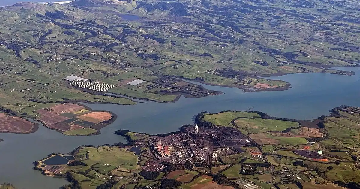 Aerial view of a steel mill beside a river surrounded by green farmland