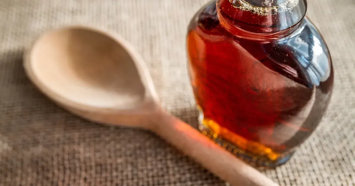 Glass bottle of maple syrup beside a wooden spoon