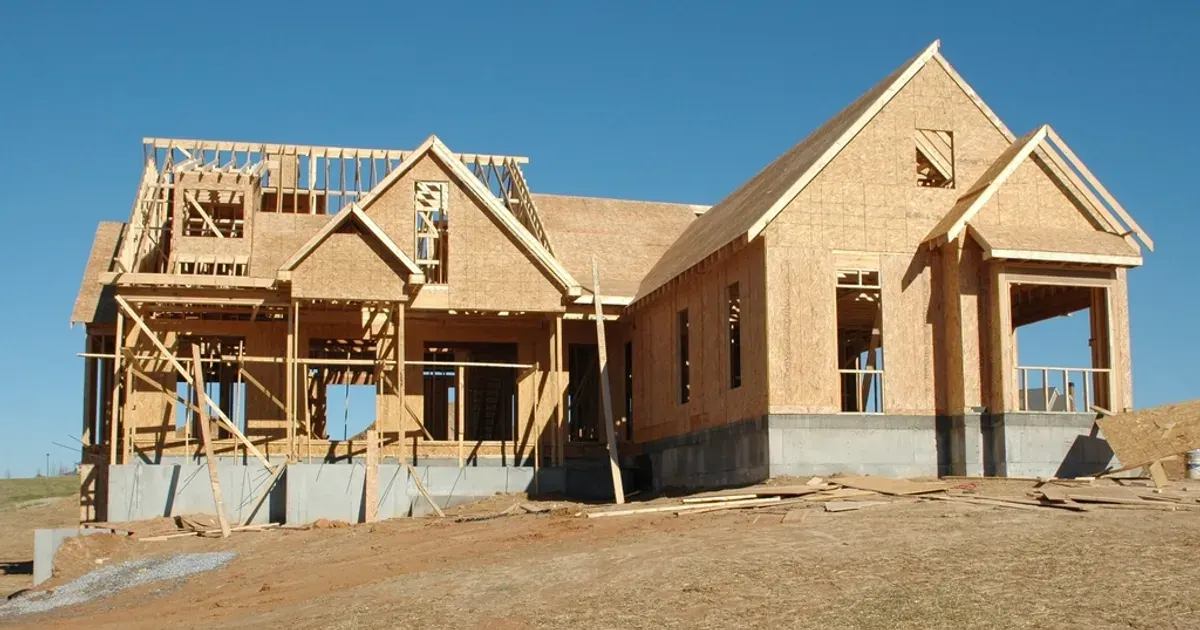 A new wood-frame house under construction on a bare lot under a blue sky