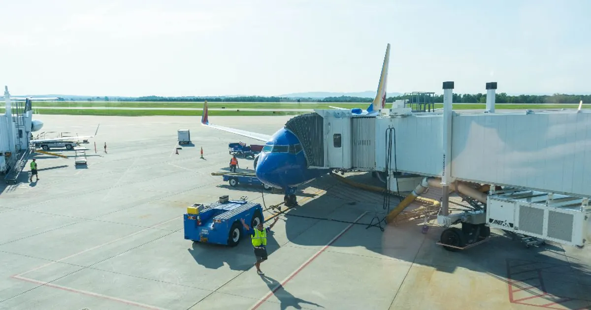 Passenger jet parked at an airport gate beside a jet bridge and ground vehicles