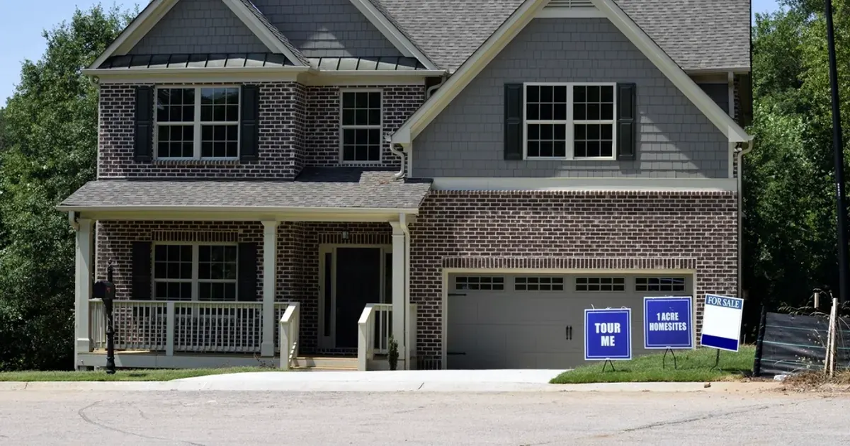 A two-storey brick and grey-siding family house with small signs on the front lawn