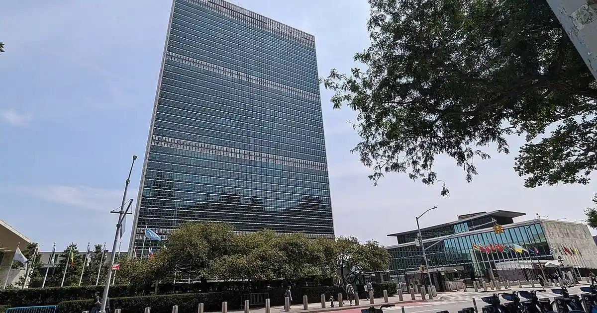 The United Nations Secretariat Building in New York, a tall glass tower, seen from the street on a sunny day