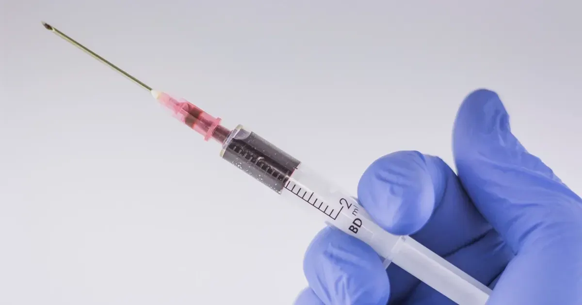 A gloved hand holding a medical syringe