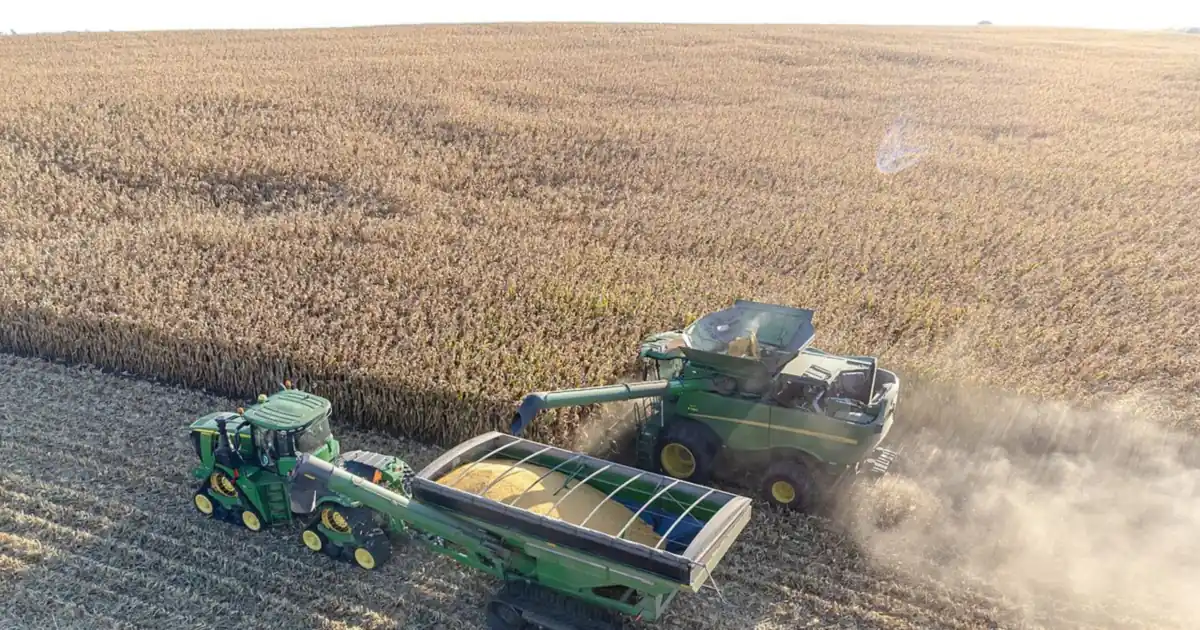 A combine harvester unloading corn into a grain cart in a farm field