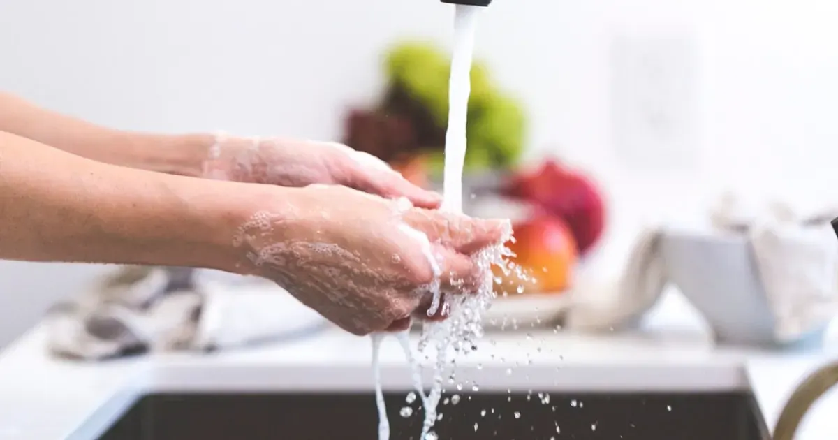 Close-up of hands being washed with soap under running water at a kitchen sink