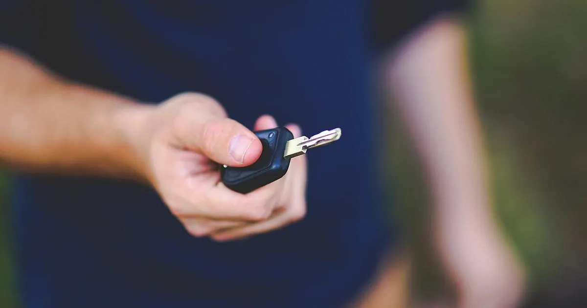A hand holding out a car key with a black remote fob