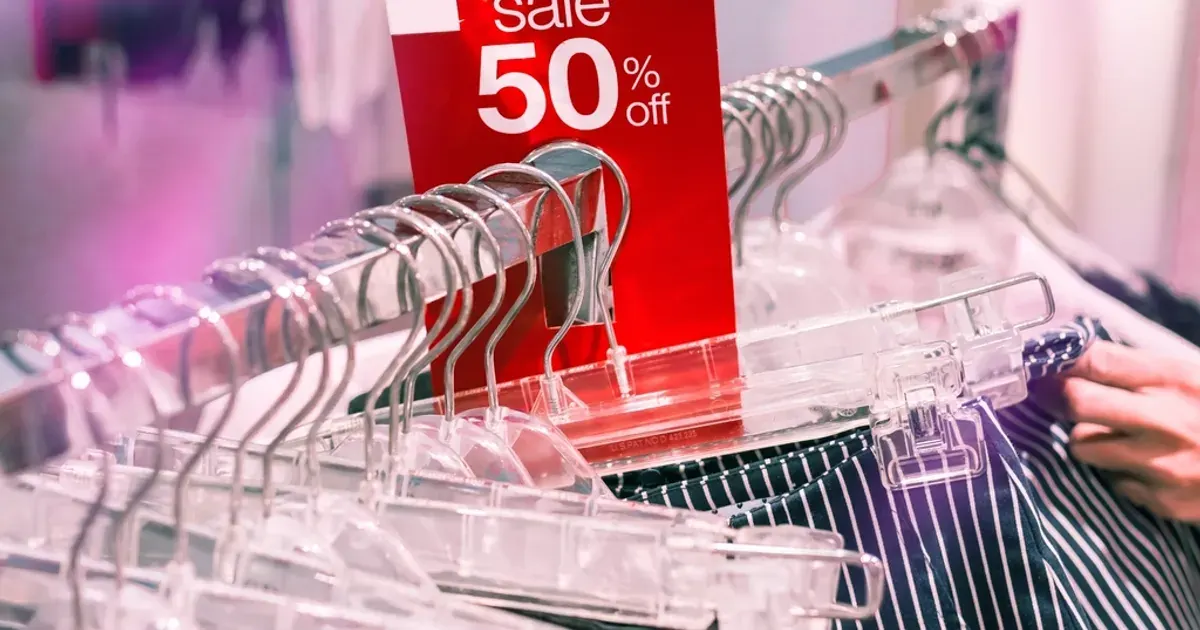 Red 50 percent off sale sign above clothes hangers in a shop