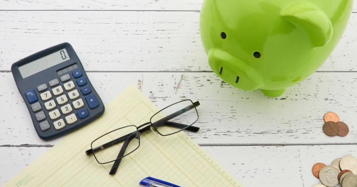 A green piggy bank, calculator, glasses and coins on a desk