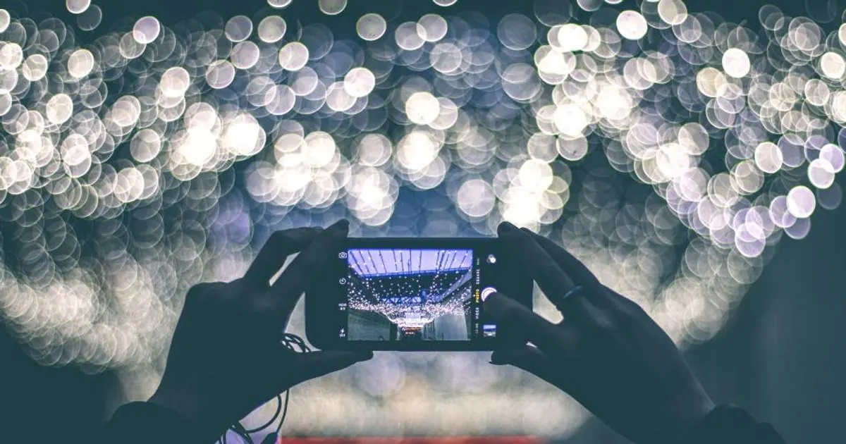 Hands holding a smartphone to photograph a ceiling of lights