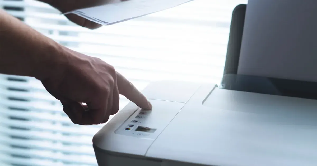 A hand pressing a button on an office printer with paper documents