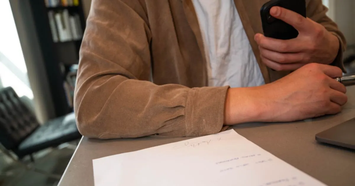 Person at a desk holding a phone next to a sheet of paper